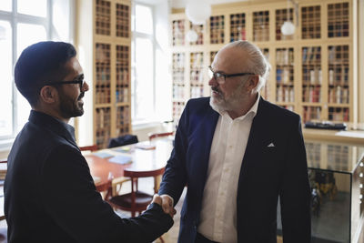 Male professional shaking hand with senior man in law library