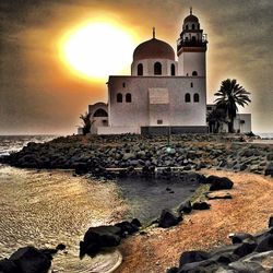 Lighthouse on beach against sky at sunset