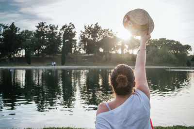 Caucasian woman from behind putting a hat to the sun in a park