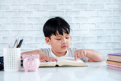 Portrait of boy with open book on table against wall