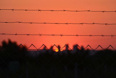 Silhouette chainlink fence against orange sky during sunset