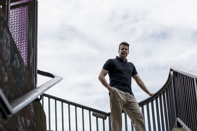 Portrait of young man leaning on railing against sky