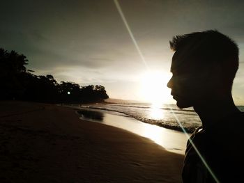 Close-up of man looking away while standing at beach during sunset