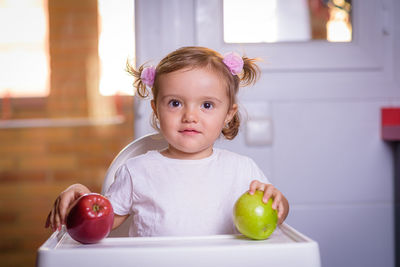 Cute baby girl with fruits on high chair at home