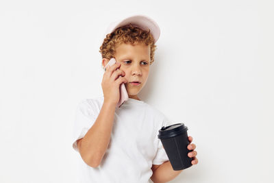 Portrait of young woman using phone while standing against white background