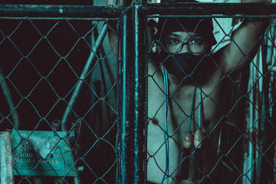 Portrait of man wearing mask seen through chainlink fence