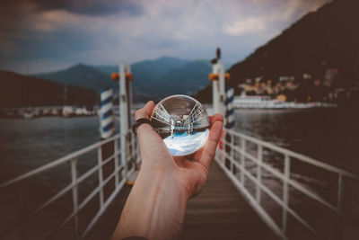 Cropped hand holding crystal ball against lake