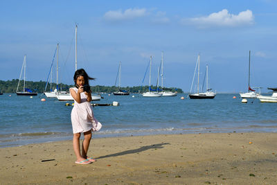 Full length of girl photographing on beach against sky