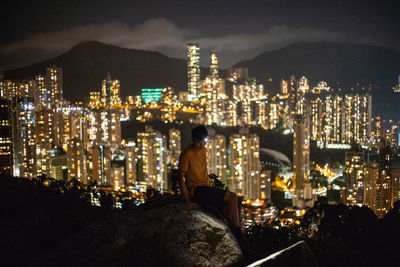 Rear view of woman sitting against illuminated buildings in city at night