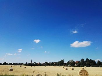 Hay bales on agricultural field against blue sky