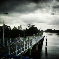 Pier on river against cloudy sky