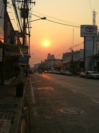 City street by buildings against sky during sunset