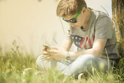 Teenage boy using phone while sitting at park