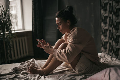 Side view of woman sitting on bed at home