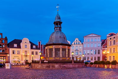 Illuminated buildings in city against blue sky at dusk