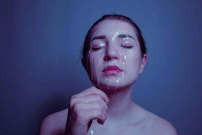 Close-up of shirtless young woman with beauty product on face against blue background