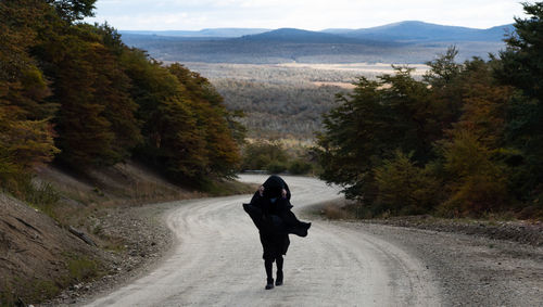 Rear view of man standing on road amidst trees