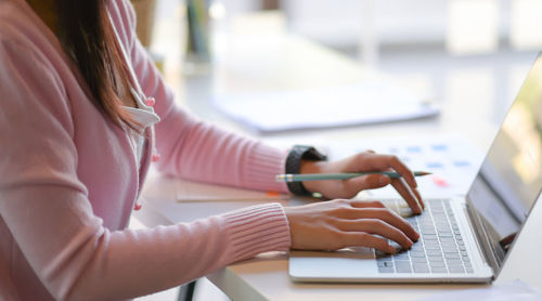 Midsection of woman using laptop at desk