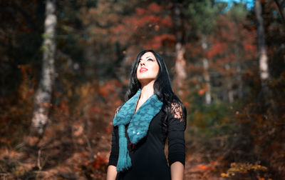 Woman looking up while standing against trees in forest