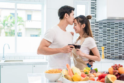 Boyfriend kissing girlfriend while standing by food in kitchen