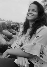 Portrait of smiling young woman on rock against sky