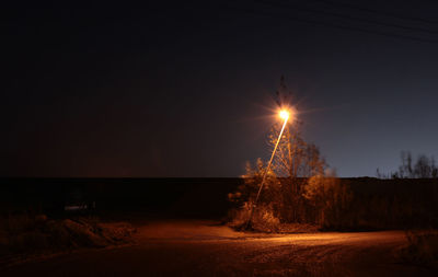 Illuminated tree by sea against sky during sunset