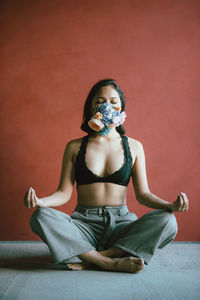 Woman wearing floral mask while mediating against wall