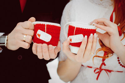 Mugs in knitted red covers with hearts with hot tea and steam in the hands of lovers