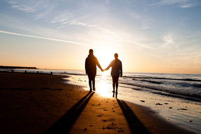 Friends on beach against sky during sunset