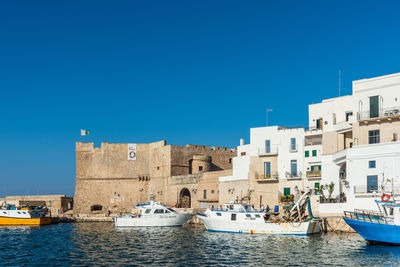 Sailboats in canal by buildings against clear blue sky