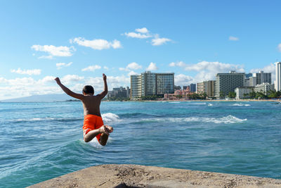 Shirtless boy jumping at beach in city
