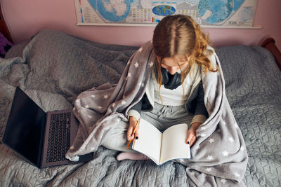 Student learning remotely from home. young woman having classes online, making notes, reading