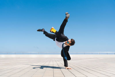 Full length of woman jumping against clear blue sky