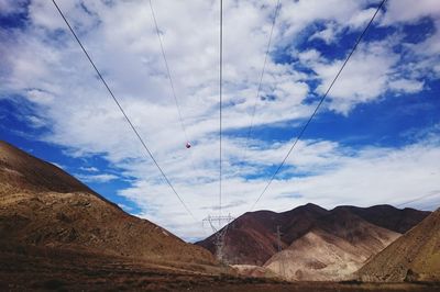 Electricity pylons amidst mountains against cloudy sky