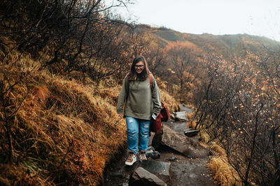 Full length portrait of young woman standing against trees