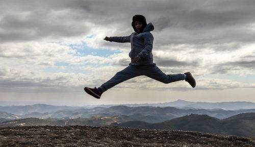 Man jumping on mountain against sky