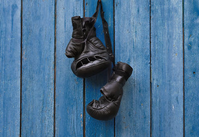 Close-up of black boxing gloves hanging on blue wood