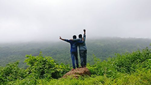 Rear view of men standing on mountain against sky