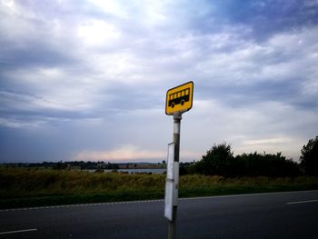 Road sign on field against sky