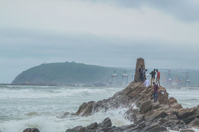 People on rocks by sea against sky at vizag 