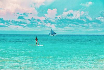 Person paddleboarding in sea against sky