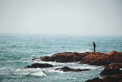 Side view of man fishing at shore against clear sky