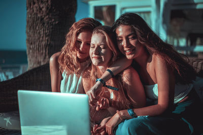 Smiling friends using laptop at beach