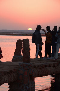 People standing on beach against orange sky