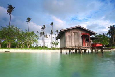 House and palm trees by lake against sky