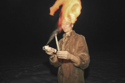 Man blowing perfume on candle while standing on snow at night