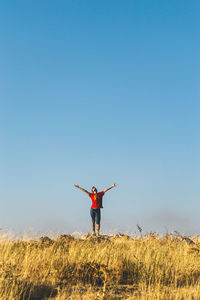 Man with arms outstretched standing on field against clear sky