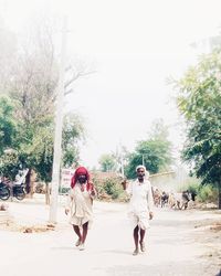 Rear view of people walking on road along trees