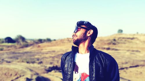 Portrait of young man wearing sunglasses standing on landscape against clear sky