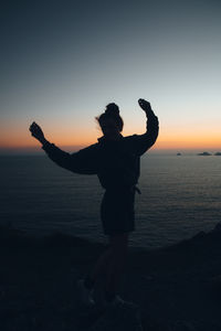 Silhouette of woman dancing on beach against sky during sunset